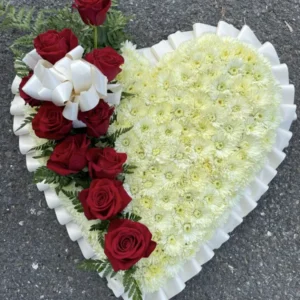 Un arrangement floral en forme de cœur, alliant lys blancs et roses rouges, symbolisant l'amour éternel. La petite jetée ajoute une touche délicate, parfait pour rendre hommage lors d'une cérémonie funéraire.