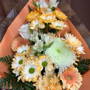 Vue de dessus d'un bouquet de fleurs fraîches "Pêche et Blanc" n°14 de Fleuriste La Romaine, composé d'une rose blanche centrale, d'un gros chrysanthème pompon blanc, de marguerites bicolores pêche et jaune, d'alstroemerias blanches et de fougères, le tout dans un emballage papier pêche avec des rubans.